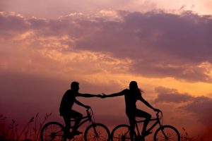 A couple is relishing a bicycle ride together in the soft glow of sunlight, holding hands as they enjoy their journey.