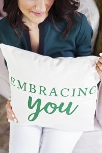 a woman holding a pillow with Embracing you written on it