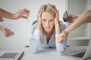A woman sits at a desk during a job interview, her hands on her head, while everyone fires questions at her.
