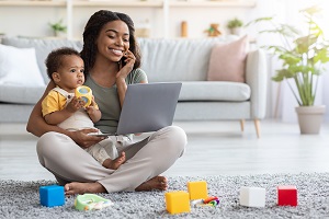 Remote Business. Portrait Of Happy Black Woman With Baby Working With Laptop And Cellphone At Home, Busy Young African American Lady Using Laptop And Mobile Phone For Online Work, Copy Space