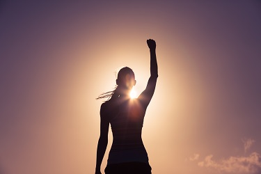 a woman standing on top of a mountain with her arms raised with sun rising towards her
