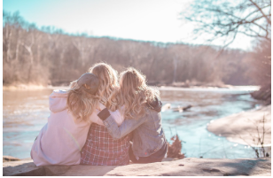 group of girls sitting and enjoying their time on a rock by a river
