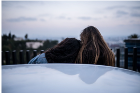 A couple is seated ahead of the car in front of their house, savoring a peaceful moment together.