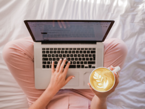 a woman is sitting on a bed with a laptop and a cup of coffee