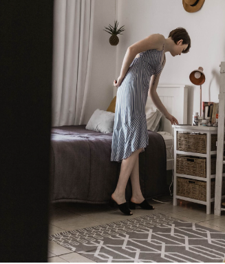 A woman wearing a blue and white striped dress is standing and searching for something in her cupboard.
