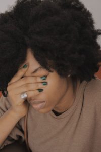 Woman covering her face and looking down. This photo could represent a person experiencing depression and sadness. Therapy for mood disorders in Woodland Hills CA can help with coping with depression using cognitive behavioral therapy.
