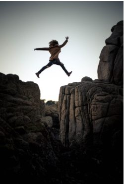 A person fearlessly jumps into the air from a rock.
