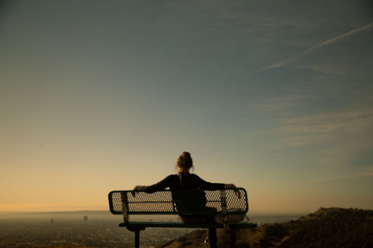 A woman is sitting on a bench looking at the sunset across the city. Learn how to set boundaries in therapy sessions that are offered at our Woodland Hills, CA therapy practice through virtual or in person sessions. 91364 | 91307 | 91356