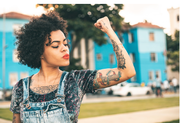 A woman with tattoos all over her body wears a blue shirt and appears self-assured as she focuses on herself.

