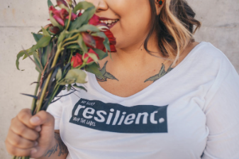 In this image we see a woman wearing a t-shirt that says "resilience" on it. The woman is holding a bouquet of flowers and is smelling them. Treating your regrets as lessons can help you move on from your past mistakes. In person and virtual therapy is offered at our therapy clinic in Woodland Hills, CA. 