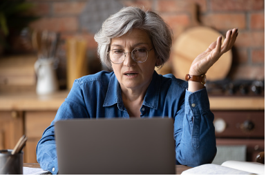 Older woman with short white hair, wearing glasses, looking at her open laptop screen in distress with her hand out. This photo could represent someone experiencing a midlife crisis trying to figure out their career goals. In person and virtual therapy is offered at our Woodland Hills therapy office. 91364 | 91307 | 91356