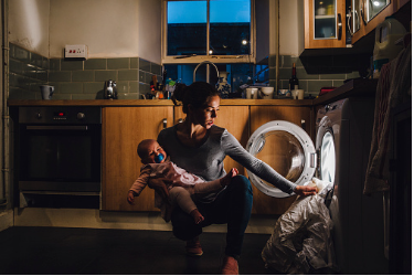 Mom is holding an infant late at night doing laundry. Mothers struggle with multi-tasking, burnout, and mental load. Therapy for maternal health in our office in Woodland hills CA or online can help you with stress management and coping skills. 