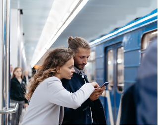 A woman leaning over a man and pointing to his phone while they stand waiting for the subway. You can learn communication skills in couples counseling to improve the bond and intimacy in your relationship in our offices in Woodland Hills CA 91307. Call today for marriage therapy.