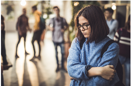 Teenage girl with glasses and short black hair is seen crossing her arms while her friends are in the distance looking at her. Losing friends or changing friend groups can be a sign of teenage anxiety worsening and can be helping by anxiety treatment that is offered at our therapy office in Los Angeles, CA. 91356 91301
teen's anxiety