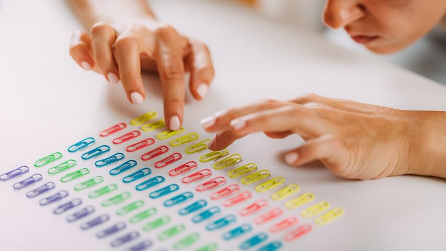 Image shows a woman lining up paperclips in different rows, sorting them by color. This image may depict a person who is struggling with their OCD symptoms.
