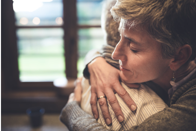 An older woman is hugging another person in their kitchen with her eyes shut. This photo could represent a person experiencing depression and sadness. Therapy for mood disorders in Woodland Hills CA can help with coping with depression using cognitive behavioral therapy. 91364