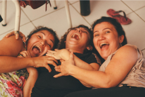 a group of female friends laying on a bed laughing and enjoying
