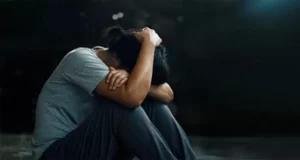 This image shows a woman hunched down on the floor with her hands over her head. This image may depict a woman who feels stressed, and is struggling with addiction recovery.