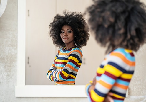 Afro Woman looking at her reflection in the mirror. Anxiety treatment in Los Angeles, CA can help with coping skills by talking to an anxiety therapist. 91301 | 91302 | 91372 91367
