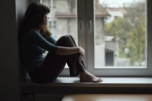 Sad young woman sitting on the window
