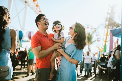 A cute mixed race family enjoys the rides and sun at the fair activities on Santa Monica Pier in Los Angeles, California.   They all wear sunglasses with big smiles. 91364