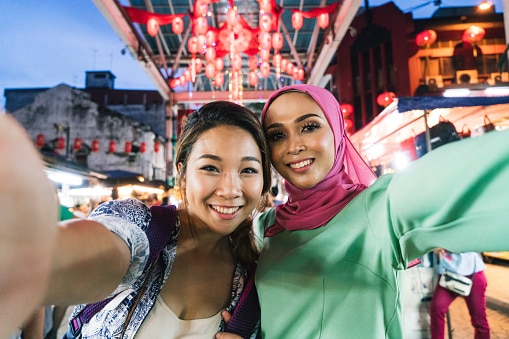 Two friends, one chinese young woman and one muslim mid adult woman,  having a selfie at the market together. 91307