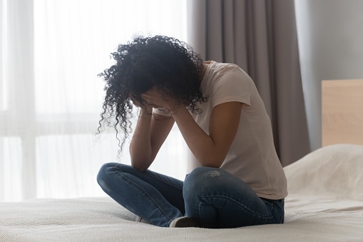 Depressed African-American woman sitting alone in bed cover face with hands crying feels desperate unhappy, concept of unrequited love, pass through divorce, abortion decision or drugs or alcohol addicted woman. CBT therapy can teach you skills to challenge your thoughts and manage depression. Call today.
