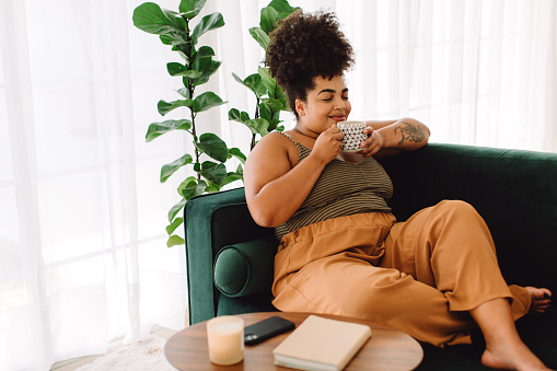 Beautiful female having coffee at home. Woman relaxing on sofa and having coffee. this photo represents utilizing coping skills to manage depression and anxiety. Feeling better and more hopeful is possible with help from an anxiety therapist in Los Angeles, CA for anxiety treatment via online therapy in California.