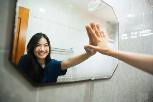 Young adult smile asian woman practice self talk conversation in the morning in bathroom at home. Hand hi-touch at mirror. Healthy lifestyle after wake up concept. 91301 | 91302 | 91372