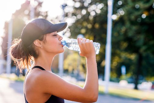 Photo of young Woman drinking water from bottle. Caucasian female drinking water after exercises or sport. Beautiful fitness athlete woman wearing hat drinking water after work out exercising on sunset evening summer,outdoor portrait. 91364 | 91307 | 91356 | 91301 | 91302 | 91372
        91367 