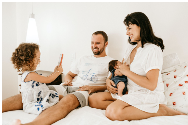 The family photo where husband, wife, their toddler daughter, and infant son is sitting on their bed in the morning where everyone is smiling. The toddler is taking a photo of the family while the mom is breastfeeding her infant son. You can also get help for anxiety counseling in Los Angeles, CA and with online therapy in California. 