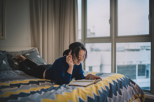 an asian Chinese female teenager lying on bed having fun writing and studying. You can get help and anxiety treatment in Los Angeles, CA with a skilled Anxiety therapist via online therapy in California here. OCD, or obsessive compulsive disorder, can also be helped here as well. 91364