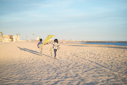 Two Filipino siblings fly their kite together on a beautiful California beach. There is no one else on the beach. There are palm trees and houses in the background. Individual therapy counseling for teens and adults in Woodland Hills, CA. 91364 | 91307 | 91356 | 91301 | 91302 | 91372 | 91367 