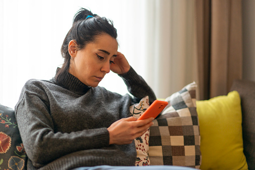 Woman sitting on a sofa and looking at mobile phone screen at home. Couples therapy and marriage counseling in Los Angeles, CA can help you feel connected. Meet with an online marriage counselor in Woodland Hills, CA with online therapy in California here.  91364 | 91307 | 91356 | 91301 | 91302 | 91372 | 91367 
