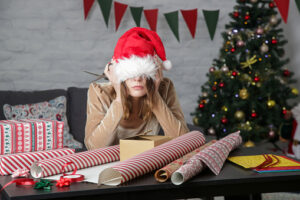 Depressed frustrated woman wrapping Christmas gift boxes, winter holiday stress concept.