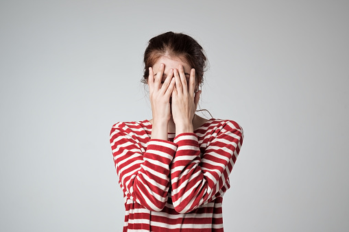 A caucasian girl covers her face with her hands, feel overwhelmed and scared for the future and the changes. If you are struggling with making decisions, starting a goal and following through, our anxiety therapist can help you to learn time management skills to set goals and take actions in your life. 
   This photo could represent someone who is thinking about things to leave in 2022. 
   90077 | 91324 | 91364 | 91411 | 91436  