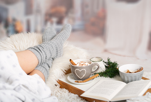 Woman lies with Cup of Hot chocolate; marshmallows; Book tray; Bed; Sofa; Blanket; Snuggle blanket; Fur; Fireplace; Wind light; Indoor; Living room; Cosy; Reading; Enjoying; Relaxing; Winter time. Turn Holiday Chaos Into Holiday Joy. You can gain new skills to feel stronger about yourself. CBT therapy in Woodland Hills, CA in person or online anywhere in California too.  91326 | 91303 | 91307 | 91377 | 91320 