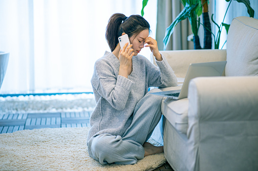 Stressed woman working at home on laptop while on the phone and has one hand on her forehead. Anxiety treatment in Woodland Hills, CA can help with coping skills by talking to an anxiety therapist. 91302 | 91372
