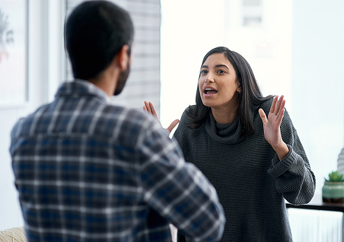 Shot of a young couple having an argument at home as the woman have her hands up and the man has his arms crossed. Therapy for mood disorders in Woodland Hills, CA can help with coping with depression using cognitive behavioral therapy. 93020 | 94513 | 91356 | 91020 