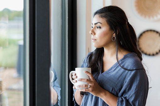 The mid adult woman takes a break with a hot drink in a mug.  She is standing at the sliding glass doors and thinking. 
        
        Therapy can help you Learn to forgive yourself.  Call today for therapy in Woodland HIlls, CA 91307