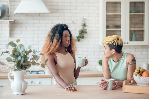 Two young adult concerned girlfriends in casual clothes communicating drinking coffee in kitchen at home. A couple's therapy can help you repair trust, improve communication, and expand your shared interest. Call today for marriage counseling in Woodland Hills. 91356 | 91301 | 91302 | 91372 | 91367