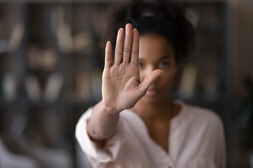 Close up focus on female mixed race palm hand showing stop sign, serious african american woman protesting against bullying in society, sexual or racial discrimination, denying family abuse indoors. 