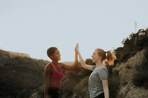 Two friends on a hike in the hills, giving each other high fives as they are smiling. This photo represents engaging in replacements behaviors to manage and reduce social media use.