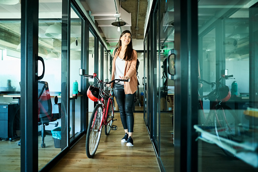 Young businesswoman pushing her bicycle and passing cubicles in the office. Therapy for mood disorders in Woodland Hills CA can help with coping with depression using cognitive behavioral therapy. 91364