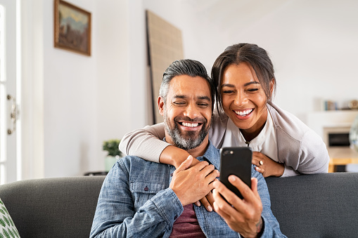 Mature multiethnic couple at home using smart phone together and smiling. Mid adult man relaxing on sofa and showing new app to african american wife on cellphone. Middle eastern man and woman sitting on couch at home and using mobile phone to do a video call with family or friends. You need to learn how to repair and reconnect after an argument to keep your couple's relationship strong and stable. You can also get help from couple's counseling in Woodland Hills, CA and with online therapy. 91364