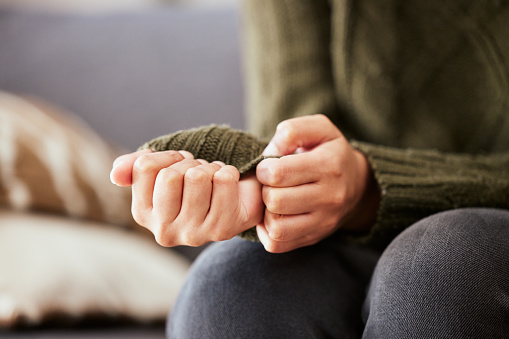 In this photo, we see a close-up shot of a womans hands. She is wearing a forest green long sleeve sweater, and is playing with the ends of her sleeves. Her hands on resting on her knees, as she nervously fidgets with her hands.