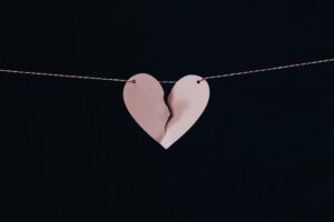 In this image, there is a paper heart that is being ripped apart as it hangs from a thread.