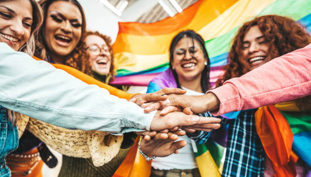 LGBTQ+ group of people stacking hands outside - Diverse, happy friends hugging outdoors - Gay pride concept with a crowd of guys and girls standing together on a city street.