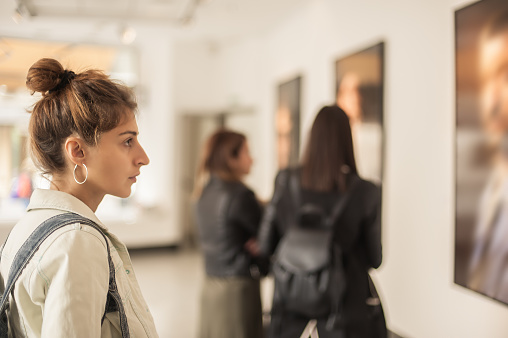A group of 3 women are at an art gallery looking at paintings. 