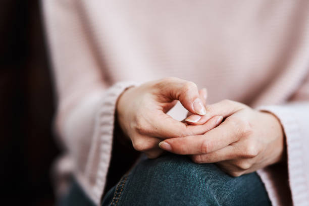 In this image, we see a close-up view of a womans' hands. Her hands are placed on her lap as she fidgets with her thumbs together.